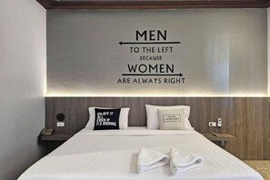 A hotel room with a bed, pillows, a bedside table, and a wall with a directional sign. - Paramount Palace Hotel Dannok (Sadao)