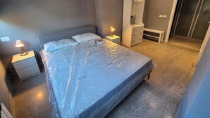 A bedroom with a bed covered in plastic, a bedside table with a lamp, a wardrobe, and a bench. - Appartamento al Centro di Roma Esquilino Colosseum Vicino Metro (Roma)