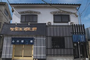 A building with a signboard, a gated entrance, and a blue banner. - Kokoro No Sato・Hitomi (Kyoto)