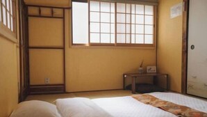A room with a bed, a small table, a window with a grid pattern, and a door with a paper on it. - Kokoro No Sato・Hitomi (Kyoto)