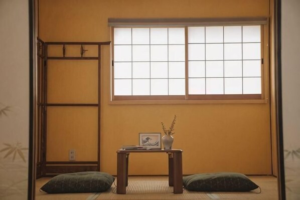 A traditional Japanese room with tatami flooring, a low table with a vase and picture frame, and a window with a grid pattern. - Kokoro No Sato・Hitomi (Kyoto)