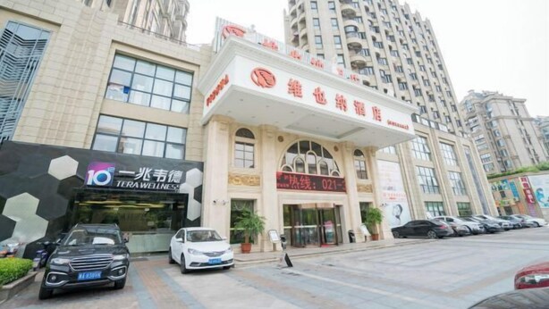 A hotel entrance with a modern facade, a visible reception area, and a parking lot with several cars. - Lvtu Zhijia Apartment Hotel (Shanghai)