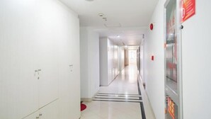 Un couloir propre et bien éclairé, avec des murs blancs et un sol carrelé, qui mène à une porte au fond.
