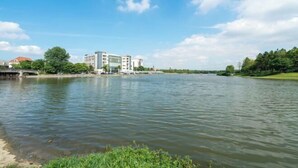 Une rivière bordée de bâtiments sur la rive opposée, un ciel dégagé et une végétation luxuriante le long des berges.