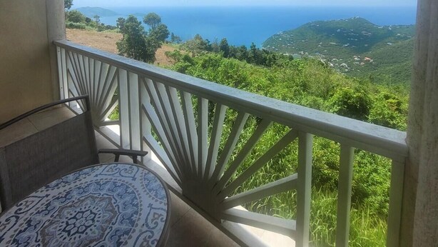 A balcony with a white railing, a patterned table, and a view of a coastal landscape with hills and the sea. - Sage Mountain Skyway 3 (Road Town)