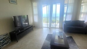 A living room with a flat-screen TV, a dark sofa, a coffee table, and a ceiling fan. - Sage Mountain Skyway 3 (Road Town)