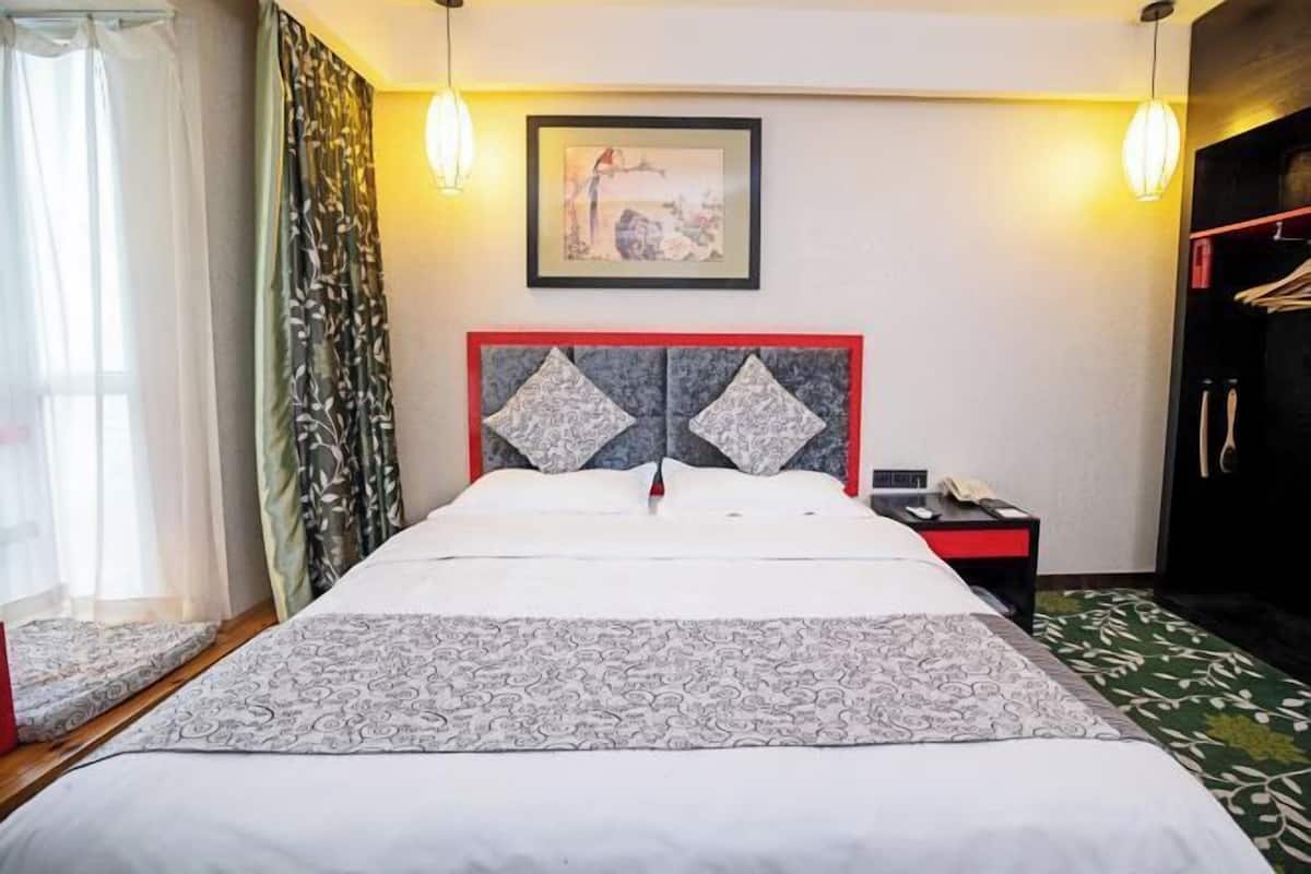 Een hotelkamer met een bed, nachtkastje, kledingkast en een schilderij aan de muur.