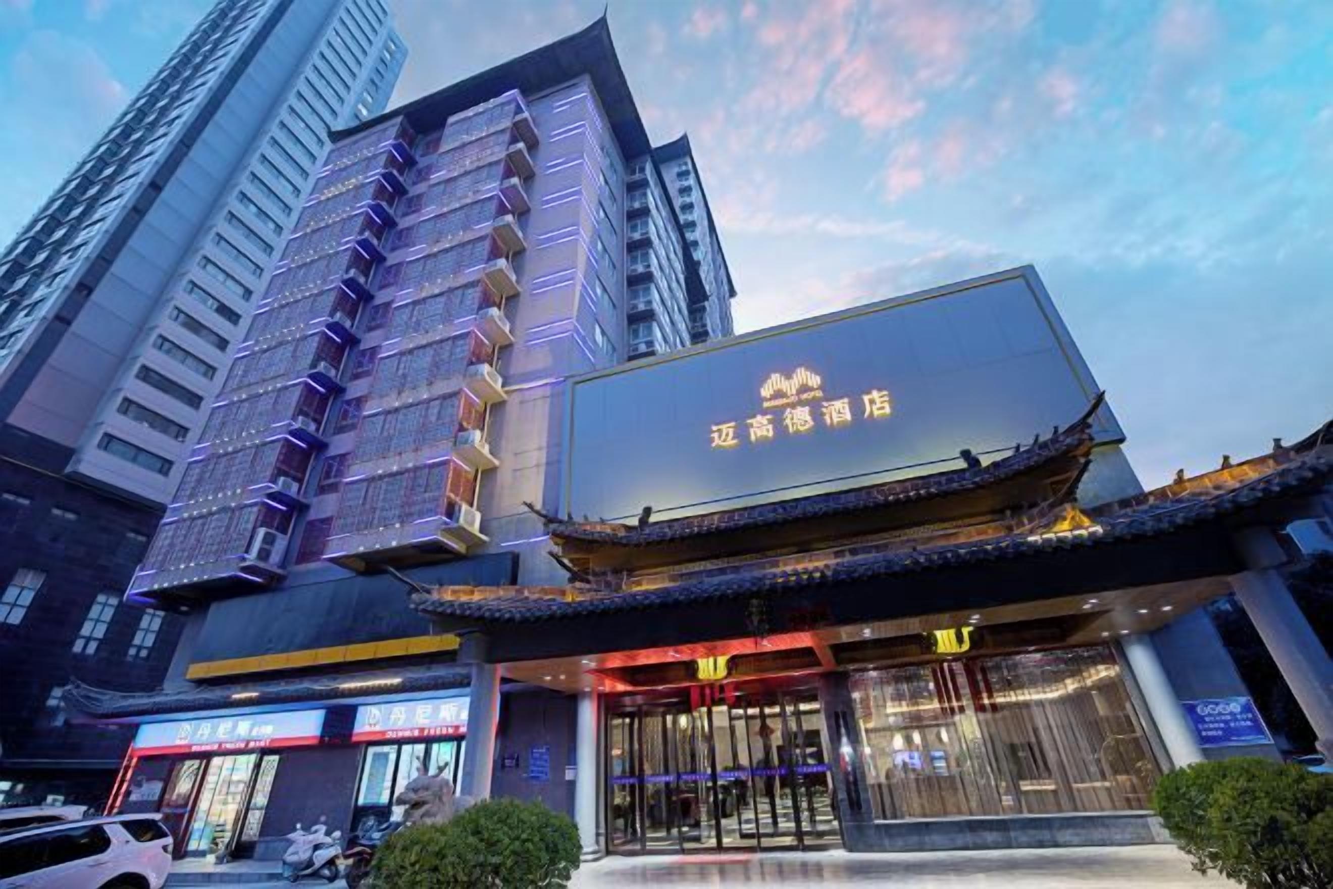 A hotel with a traditional architectural style, a large illuminated sign, and a modern building in the background.