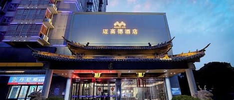 A hotel with a traditional architectural style, featuring a prominent entrance with a tiled roof and a large illuminated sign.