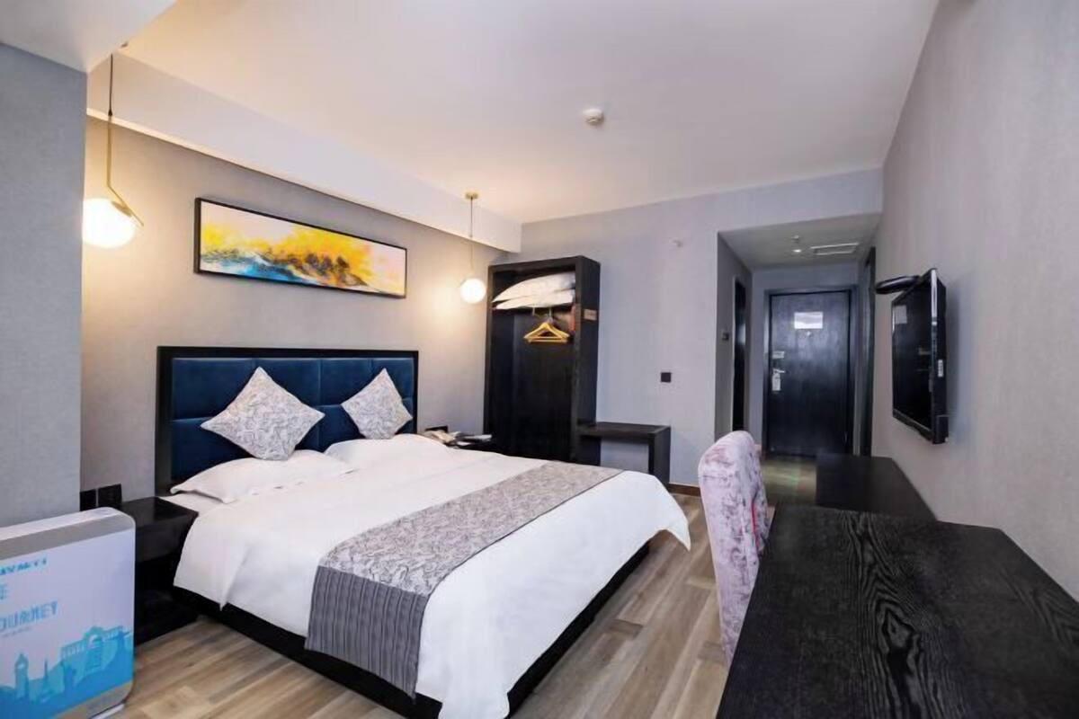 Een moderne hotelkamer met een groot bed, nachtkastjes, een bureau en een aan de muur bevestigde televisie.