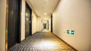 A hotel hallway with a patterned carpet, doors, and an emergency exit sign.