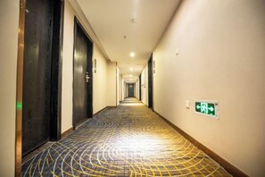 A hotel hallway with a patterned carpet, doors, and an emergency exit sign. - Maigode Hotel (Henan People's Hall Yanzhuang Metro Station) (Zhengzhou)