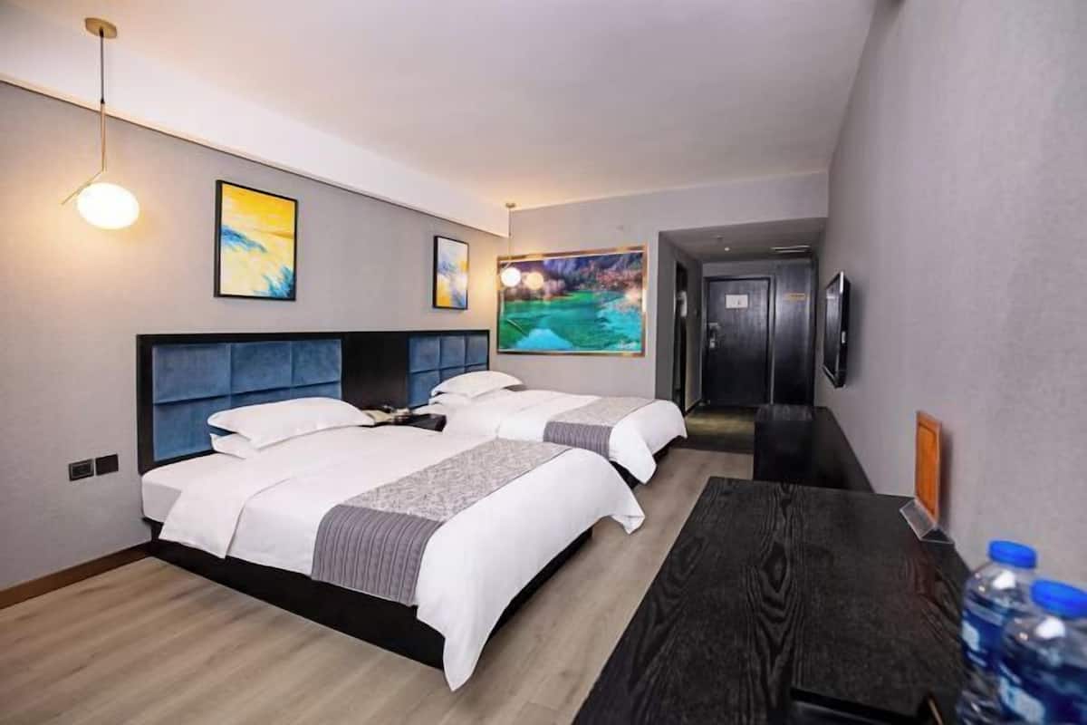 Hotelkamer met twee bedden, een bureau en een televisie. Er hangen schilderijen aan de muren en een deur aan de rechterkant.