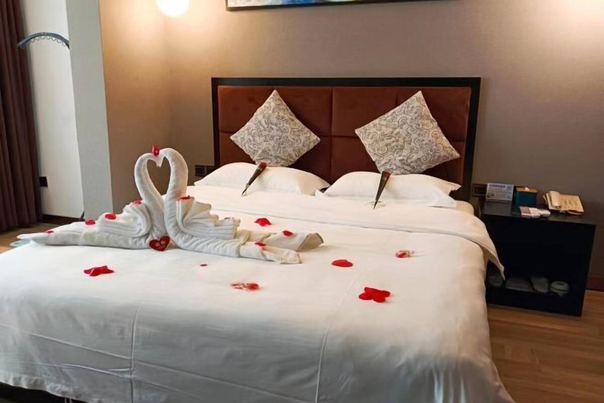 Een hotelkamer met een bed, kussens, een nachtkastje en een wandlamp.