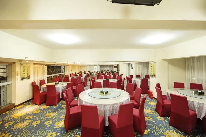A large conference room with multiple round tables and red chairs, carpeted floor, and a view of the city through the windows.