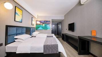 A hotel room with a bed, a TV, a desk, and artwork on the walls.