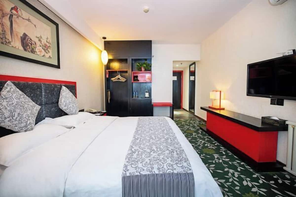 Een hotelkamer met een bed, een televisie, een rode bureau en een schilderij aan de muur.