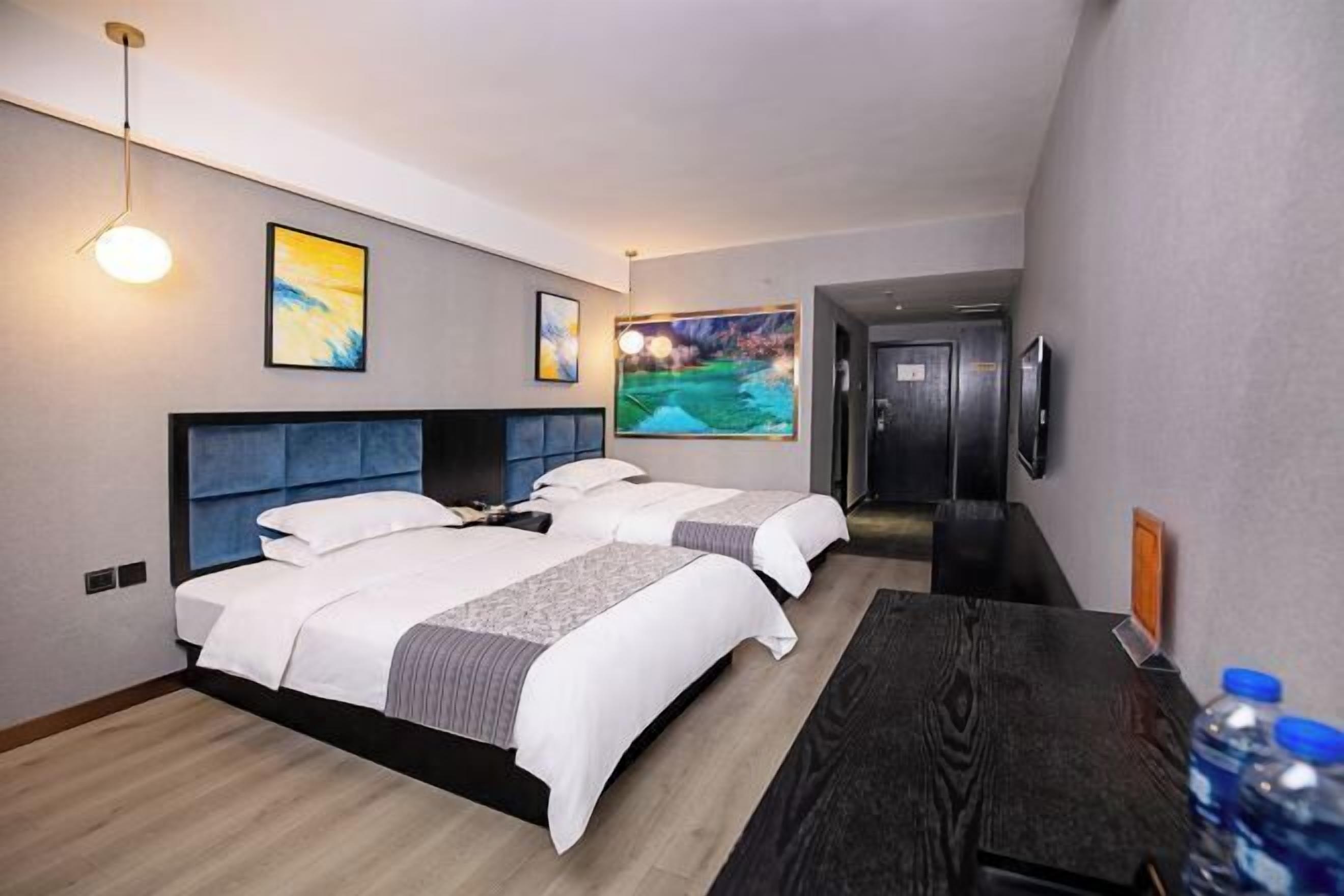 A hotel room with two beds, a desk, a TV, and artwork on the walls.