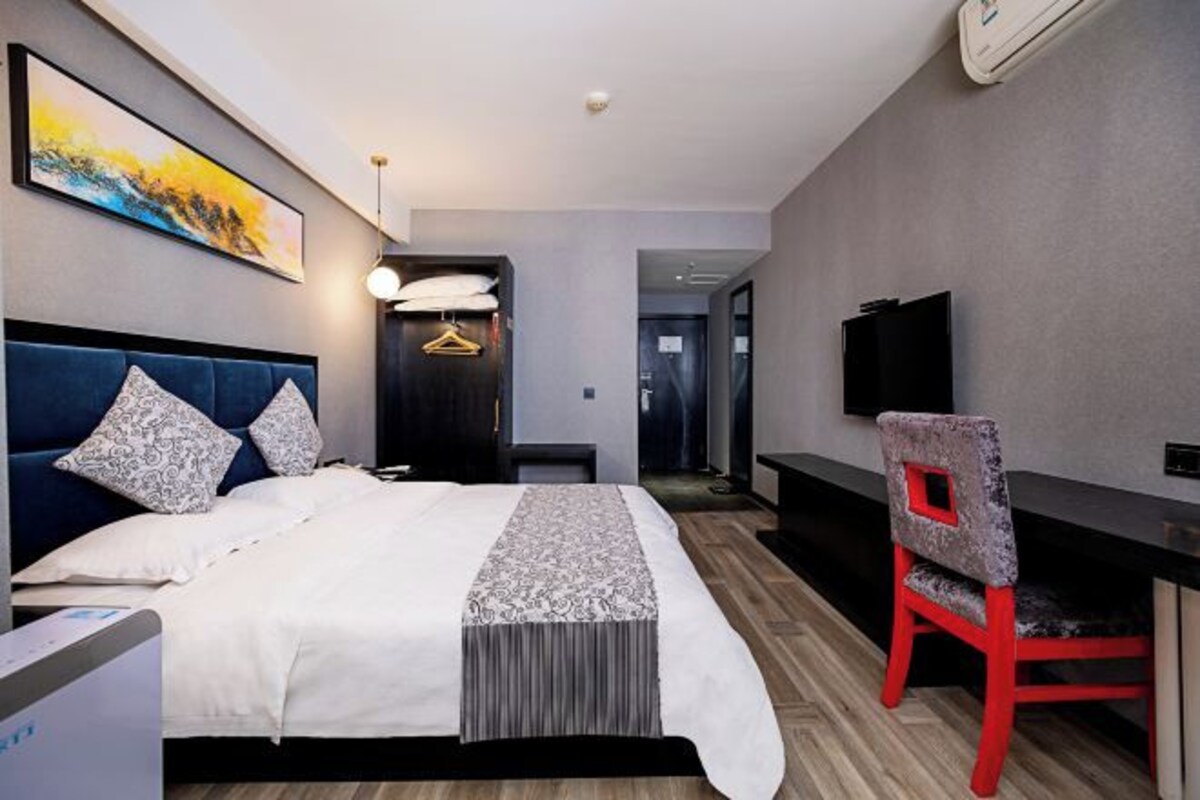 A modern hotel room with a bed, a desk, a chair, a TV, and a painting on the wall.