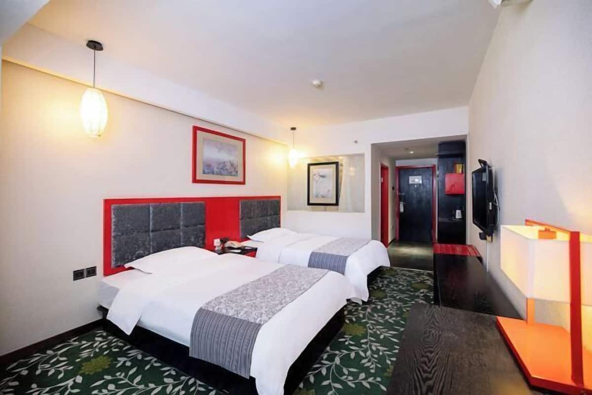 Hotelkamer met twee bedden, een rood hoofdeinde, een ingelijst beeld aan de muur, een televisietoestel en een nachtkastje.