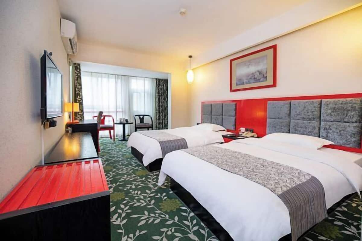 Een hotelkamer met twee bedden, een bureau, een stoel, een televisie en een raam met gordijnen.