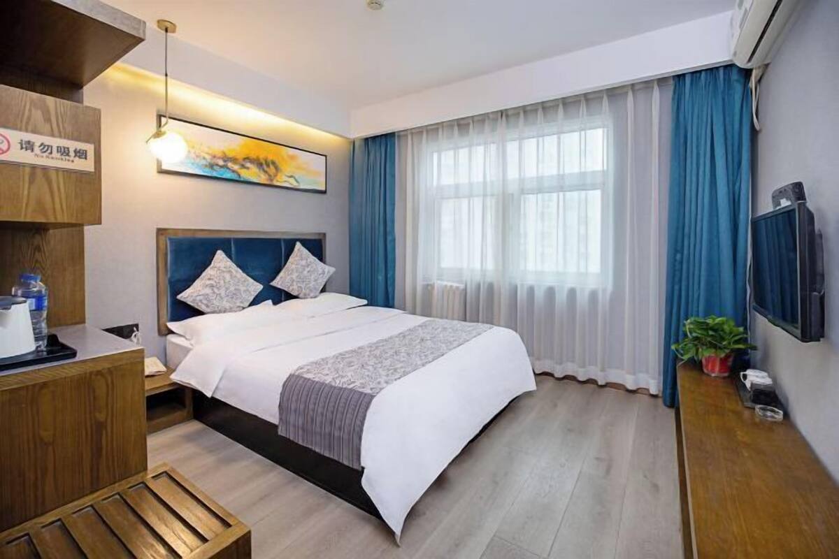 Hotelkamer met een bed, bureau, televisie, raam met gordijnen en een schilderij aan de muur.