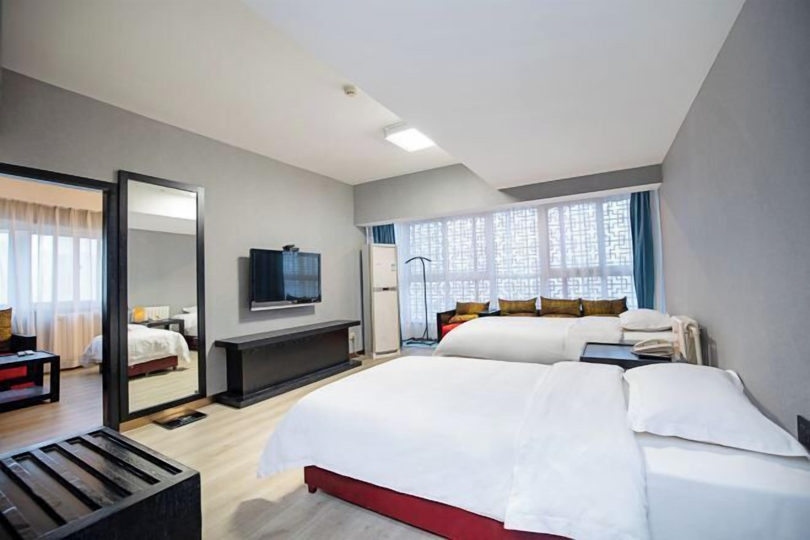 A hotel room with a large bed, a TV, a mirror, and a window with curtains.