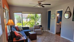 Una sala de estar con sofá, sillón y mesa de centro, un ventilador de techo y vistas al exterior.