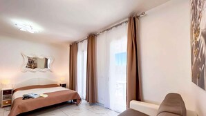 Ein Hotelzimmer mit Bett, Sofa, Nachttisch, Lampe, Spiegel und einem Fenster mit Vorhängen.