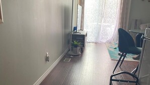 A hallway with wooden flooring, a radiator, a potted plant, a desk with a chair, and a window with sheer curtains. - Cozy one bedroom apartment  (Peterborough)