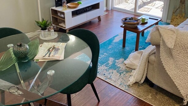 A living room with a glass table, a green chair, a TV on a white stand, and a view of the outdoors through a sliding glass door. - Cozy one bedroom apartment  (Peterborough)