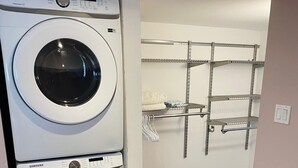 A laundry room with two Samsung washing machines, wooden flooring, and metal shelving units. - Cozy one bedroom apartment  (Peterborough)