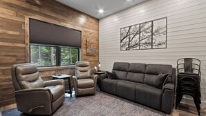A modern living room with a leather recliner, a gray sofa, and a stack of chairs. - Secluded Getaway,  Centrally located newly built barndo, AC & WIFI (Elmira)