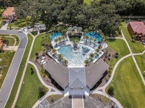 An aerial view of a resort with a central swimming pool, multiple lounge areas, and a parking lot.