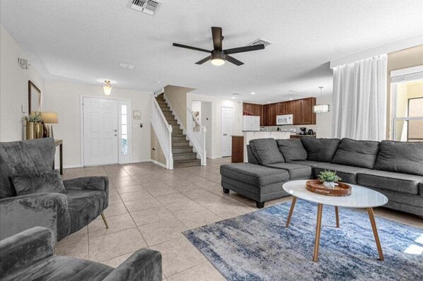 A spacious living room with a grey sofa, a coffee table, and a staircase leading to a kitchen.