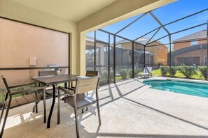 A covered patio area with a pool, outdoor seating, and large windows offering views of neighboring houses.