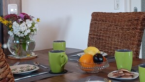 A dining table with green cups, a fruit bowl, and a vase of flowers.