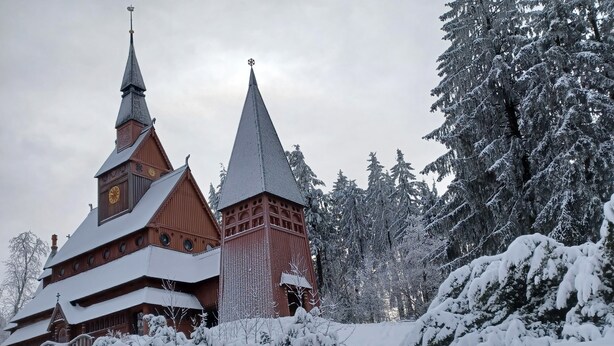 A wooden church with multiple spires, surrounded by snow-covered trees.