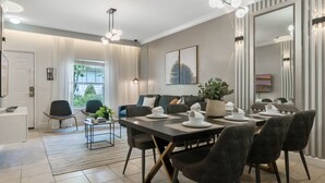 A modern dining area with a long table set for four, surrounded by dark upholstered chairs. A large mirror and a framed cityscape artwork adorn the walls. - Last Minute Disney Getaway! Townhouse with Private Pool. Book Now! #65617 (Orlando)