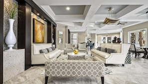 A spacious living area with a modern design, featuring a large sofa set, a coffee table, and a dining area with a chandelier.