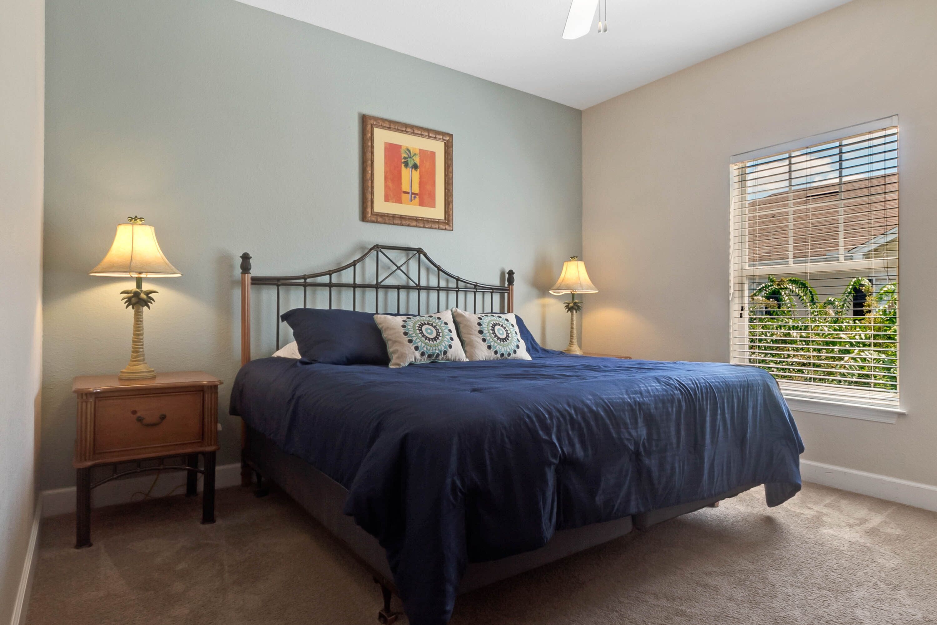 Quarto com cama, duas mesas de cabeceira, janela com persianas e um quadro pendurado na parede.