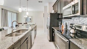 Une cuisine moderne dotée de plans de travail en granit, d’appareils électroménagers en acier inoxydable et d’un revêtement mural en carreaux.