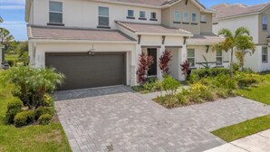 A two-story residential building with a garage, paved driveway, and landscaped garden with various plants. - Last Minute Disney Getaway! Villa with Private Pool & Hot Tub. Book Now! #116945 (Orlando)