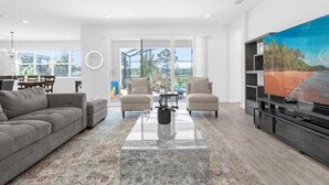 A modern living room with a grey sofa, two armchairs, a coffee table, and a TV on a black stand. - Last Minute Disney Getaway! Villa with Private Pool & Hot Tub. Book Now! #116945 (Orlando)