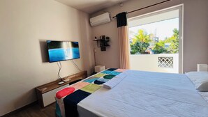 A hotel room with a bed, a TV mounted on the wall, an air conditioning unit, and a window with a view of greenery and buildings. - Charming beach apartment - 5 minutes from Pereybere beach (pereybere)