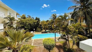 A swimming pool surrounded by palm trees and greenery, with a clear blue sky. - Charming beach apartment - 5 minutes from Pereybere beach (pereybere)