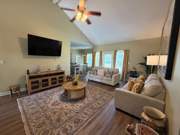 A living room with a flat-screen TV, a ceiling fan, a dining area, and a sofa.