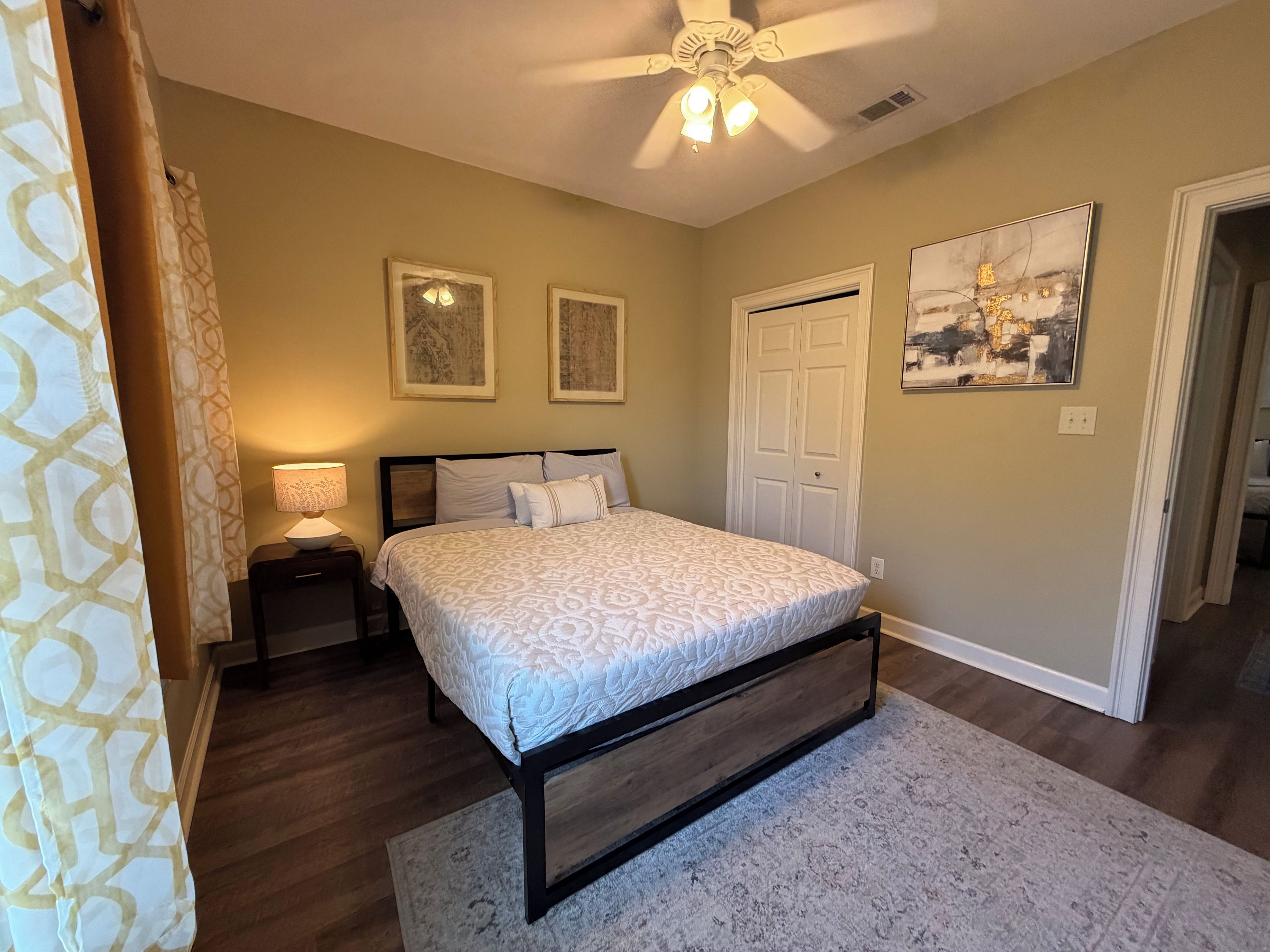 A bedroom with a bed, nightstands, a ceiling fan, a door, and two framed pictures on the wall.