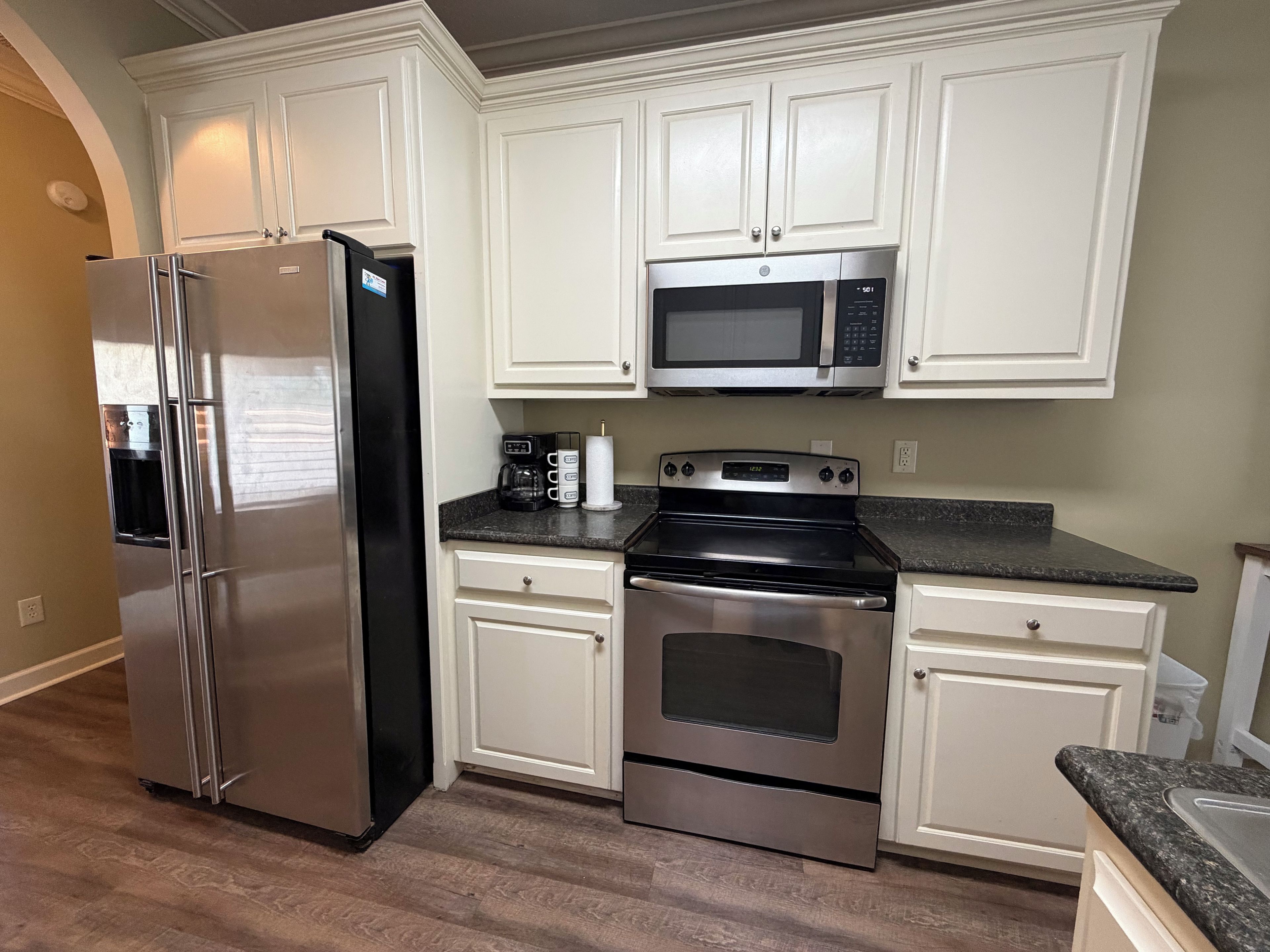 Una cocina con armarios blancos y electrodomésticos de acero inoxidable, incluyendo un refrigerador, microondas y horno.