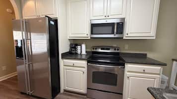 Una cocina con armarios blancos y electrodomésticos de acero inoxidable, incluyendo un refrigerador, microondas y horno.